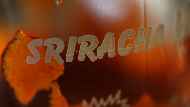 A closeup picture of a bottle of Sriracha sauce showing the brand name.