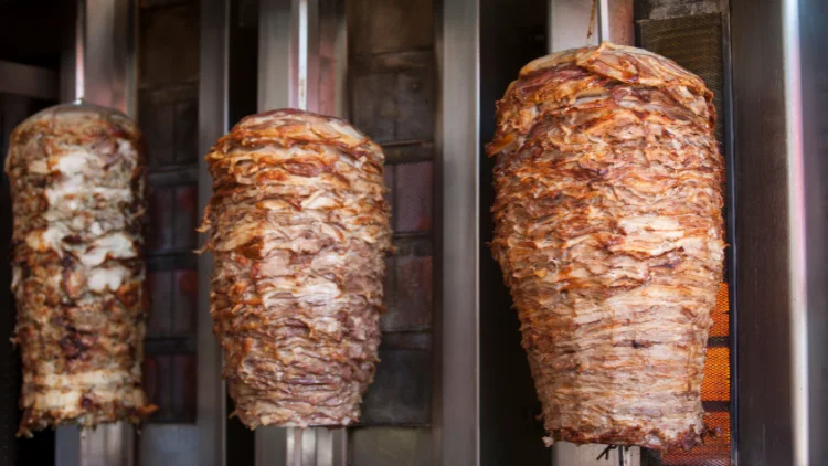Three large gyro meat cones sizzle and cook on a rotating spit.