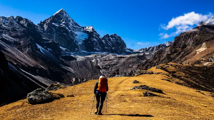 A woman wearing hiking gear and a backpack walking on a rocky mountain trail, with a stunning view of Mount Everest in the background, she is stepping confidently and appears to be enjoying the challenging terrain, the backpack on her back suggests that she may be on a mountaineering expedition or a long hike.