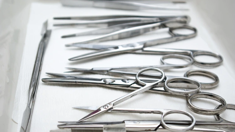 On a white sheet, there are various surgical tools that are displayed such as scalpel, scissors, and forceps.